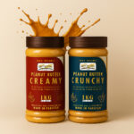 Two jars of Royal Ove peanut butter—one creamy and one crunchy—stand side by side on a dark surface, with peanut butter splashing dramatically out of the open lids. The creamy jar has a red label, and the crunchy jar has a blue label. Both “100% Organic,” “1KG,” and “Made in Pakistan.” The background features moody red and blue lighting with gym-style dumbbells, giving a bold, energetic fitness-themed look.